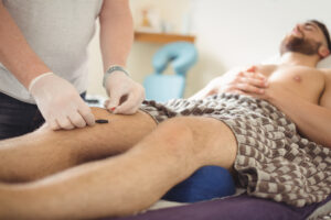 Physiotherapist performing electro dry needling on the knee of a patient in clinic