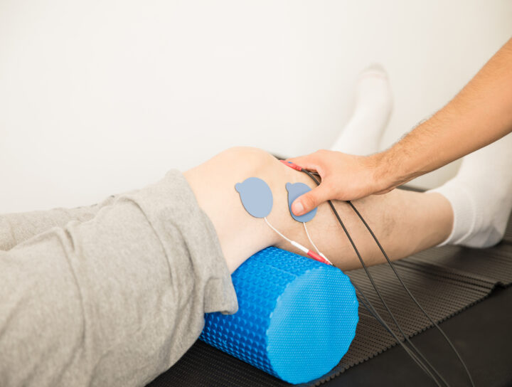 Physiotherapist's Hand Positioning Electrodes On Patient's Knee